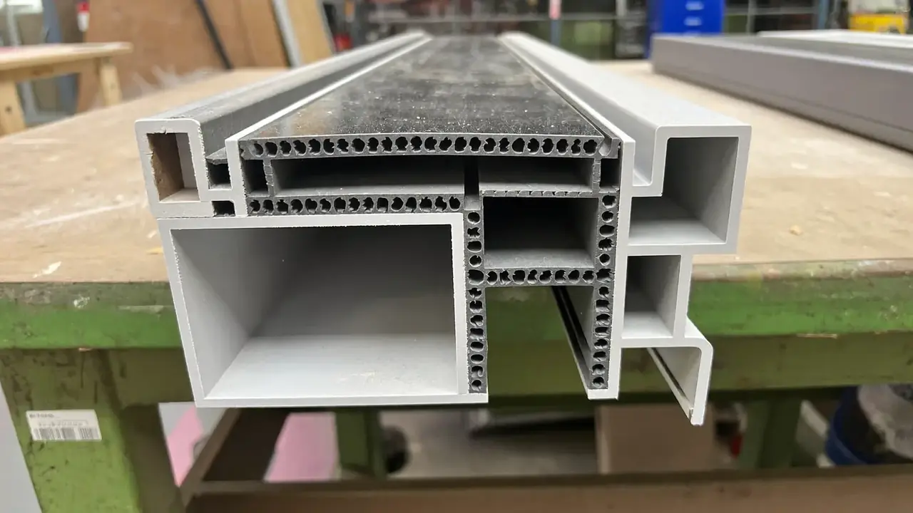 A cutaway uPVC window profile on a workbench showing internal chambers